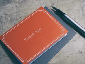 Brown note card with thank you and a pen. Donate and gifts that inspire donations.