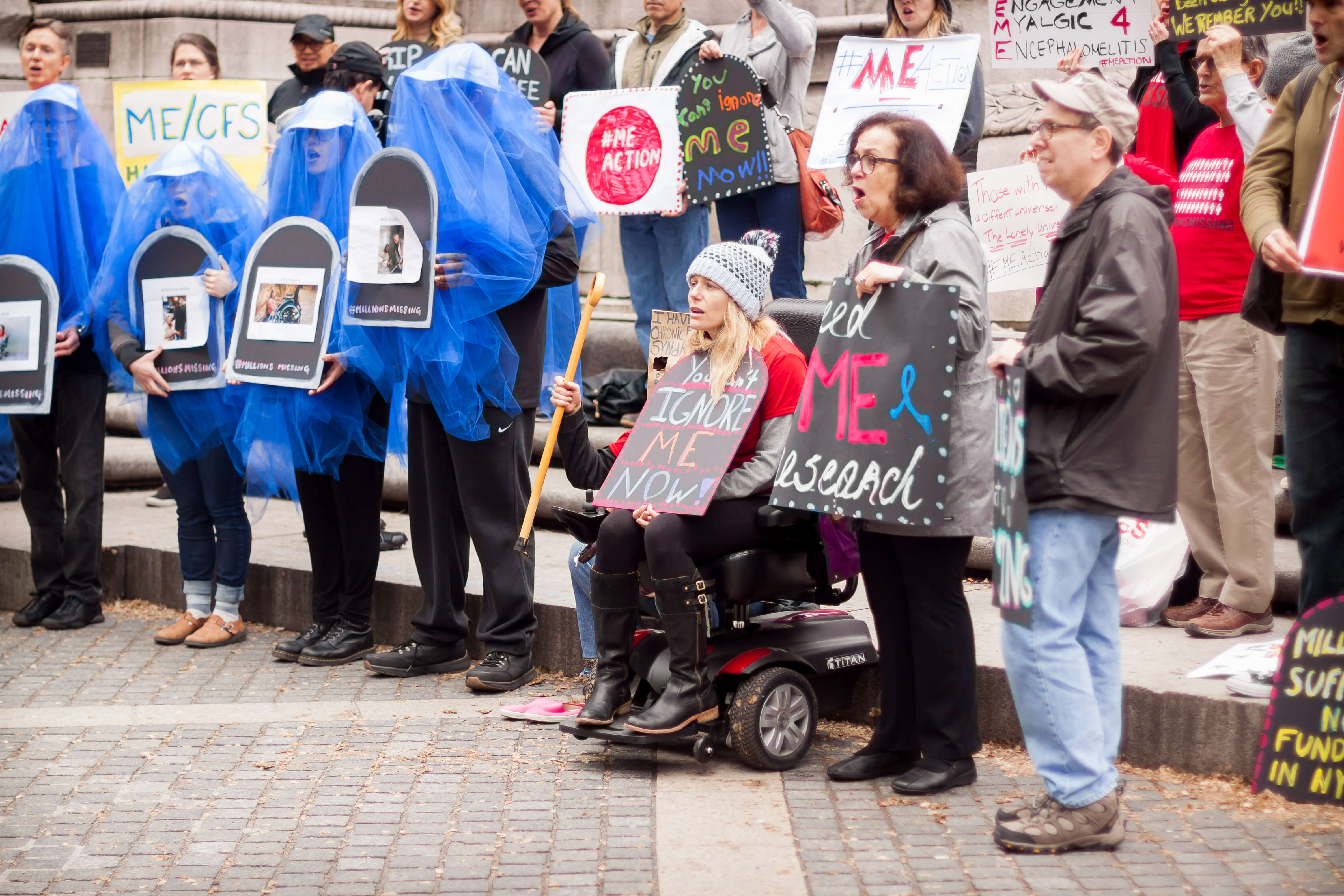 People hold up signs at ME Action Awareness Day. Copyright Stefanie Giglio. Illness. Myalgic Encephalomyelitis