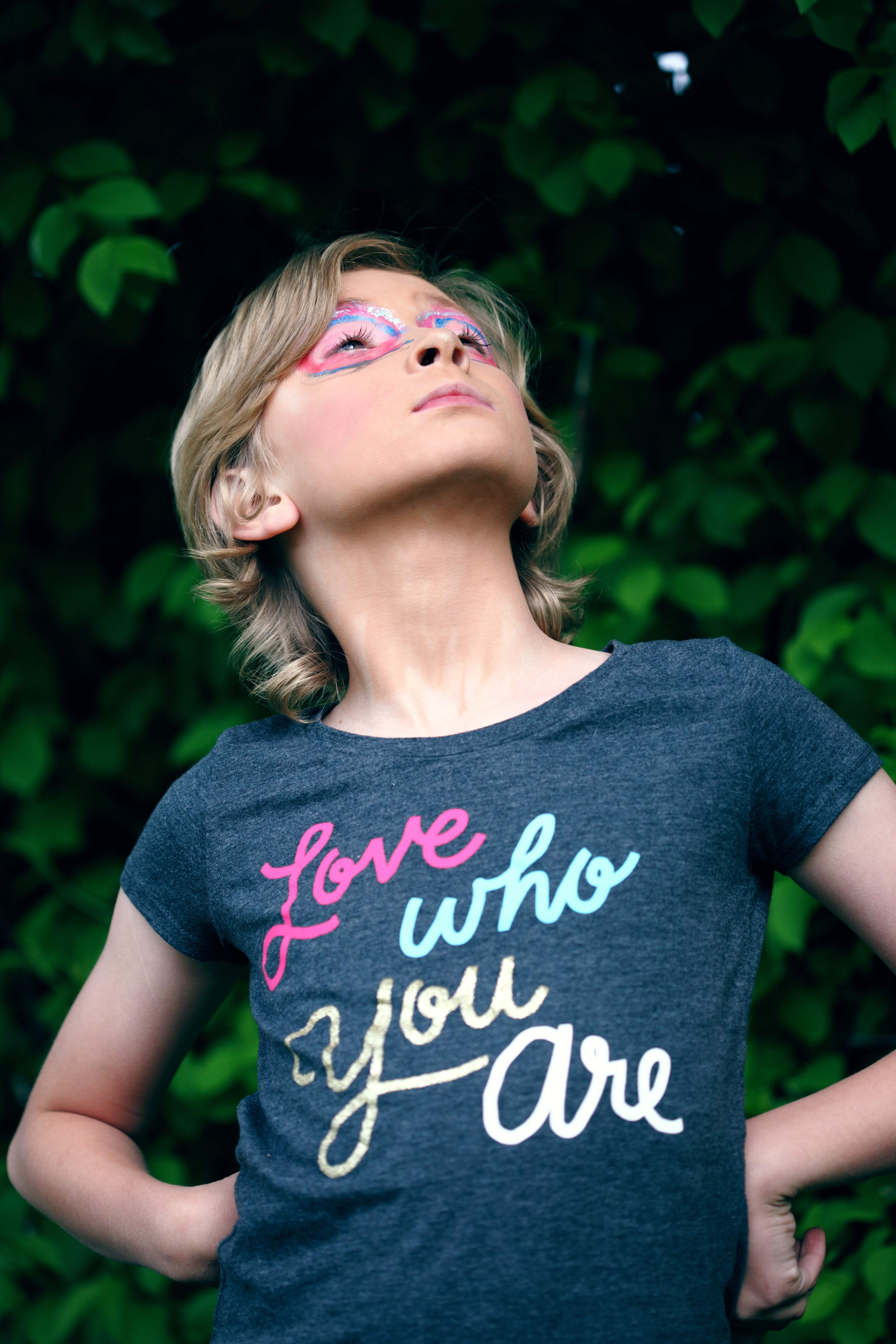 Young person wearing eye makeup and a T-shirt that says "Love Who You Are". Trans.