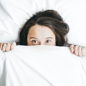 Woman in bed with white sheets peeking out. what to do when you're afraid to be an activist. feeling powerless and scared to change things.