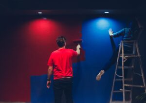 Man in red shirt paints red on a wall while a woman in a blue shirt paints blue. Patriot define