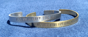 One silver and one bronze bracelet stamped with accessibility for all. Activism Gifts.