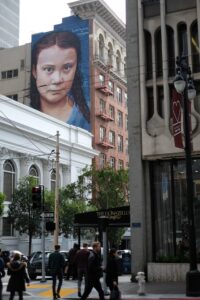 A mural of global warming activist Greta Thunberg looks over a city street.
