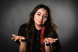 A white woman with long brown hair shrugs and holds her hands out.