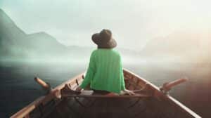 A woman in a green shirt and a wide-brimmed hat sits in a rowboat.
