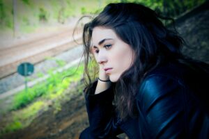 A pensive young white woman with black hair stares down a railroad track.