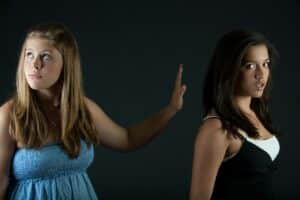 A young blonde white woman holds her hand to stop a young white dark-haired woman from speaking. How to get involved in activism. Making a difference in your community.