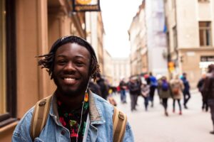 A smiling black man wearing headphones walks on a busy street. Motivational Resources and Learning Opportunities for Activists.