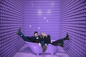 A man and a woman sitting in a bathtub in a completely purple room, having fun.