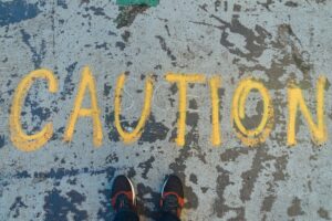 The word, "Caution" written in yellow chalk on a street, with a pair of shoes showing at the bottom. AI and activism. Artificial intelligence in social change.