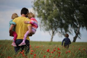A dad holds 2 kids while a third child runs ahead in a field of poppies. Turn your passion into action.