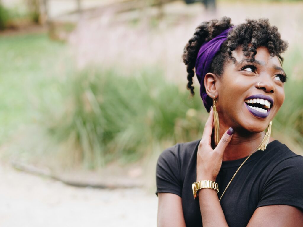 A happy young African American woman with a black shirt and a purple headband smiles broadly to the side. Inspirational.