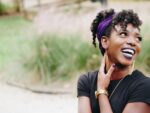 A happy young African American woman with a black shirt and a purple headband smiles broadly to the side. Inspirational.