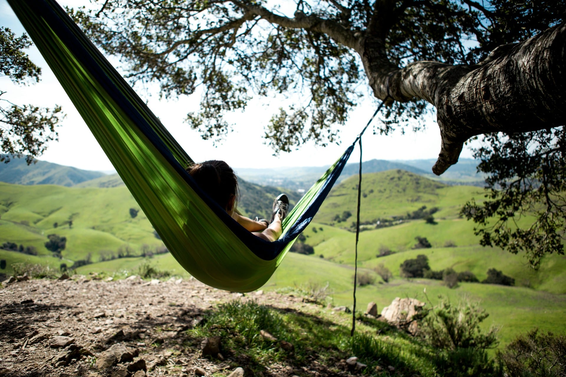 A green hammock between two trees with a person relaxing and enjoying the view. Mental health resources for healthy minds and mindfulness.