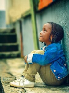 A young black girl sitting against a wall looking up and smiling. angst hopeless