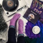 Looking down on self care kit items of comfy purple socks a latte, and music. Learn how to stay motivated and avoid activism burnout. Get a set goals worksheet.