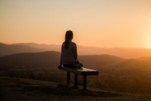 A woman sits on a bench and contemplates a sunset over the mountains. Equanimity means, the meaning of equanimity.