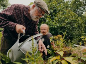 Grandfather showing granddaughter how to water a garden.