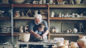 Grandfather showing grandson how to make pottery in workshop