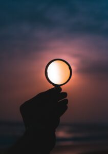 A hand holds a magnifying glass in front of a sunset. The meaning of critical thinking. Fact-checking websites.